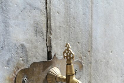 Стара чешма на каменна стена със златист кран и чучур.